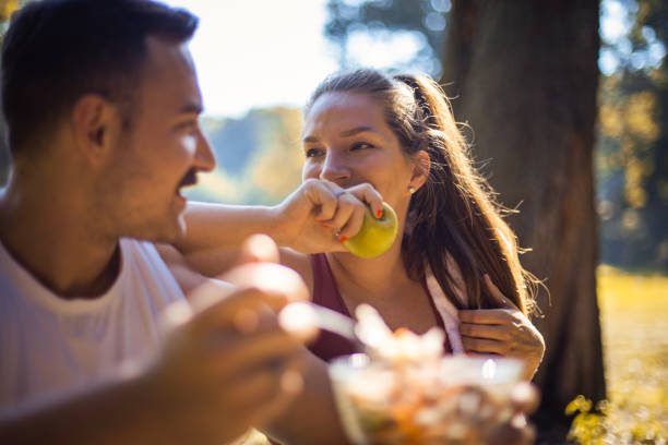 공원에서 휴식을 취하고 건강한 식사를 먹는 커플. 샐러드와 사과. 초점은 여성에 있습니다. - apple eating healthy eating friendship 뉴스 사진 이미지