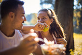 Couple in the park having break and eating healthy meal. Salad and apple. Focus is on woman.