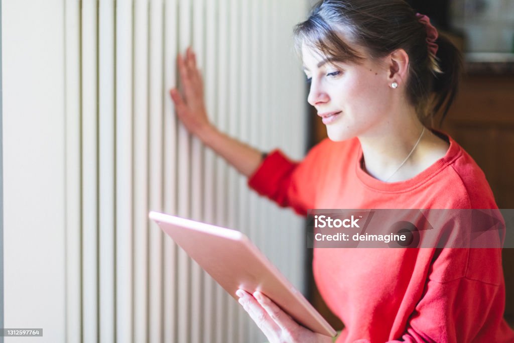 Junge Frau überprüft mit Gerät Heizkörper im Wohnzimmer von Smart Home, IOT - Lizenzfrei Heizkörper Stock-Foto