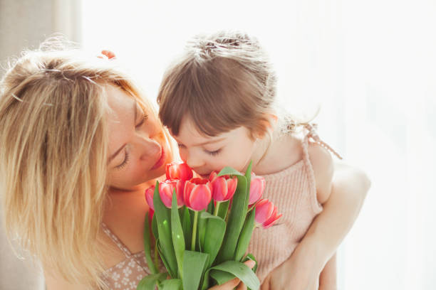 menina e sua mãe abraçando e cheirando tulipas - 5563 - fotografias e filmes do acervo