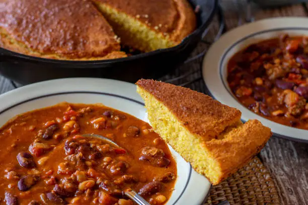 Mexican spicy bean stew with kidney beans served on a rustic plate with a piece of fresh baked corn bread from above on wooden table background