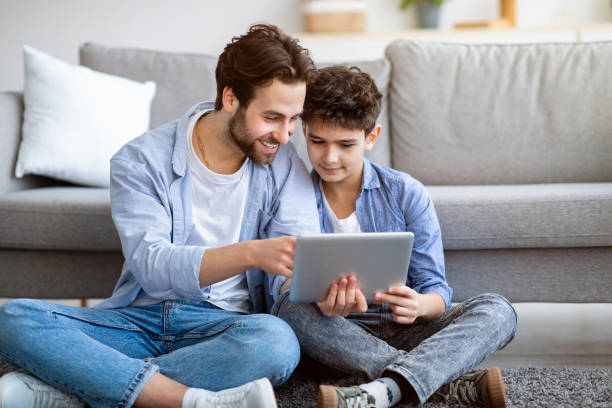 istock Father and son using tablet computer at home, checking new application, sitting on floor carpet near sofa 1312598464