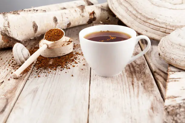 Photo of Mug of chaga tea on wooden table in a rustic style. Nearby are lied natural Chaga birch mushrooms. Healthy beverage is used in alternative medicine
