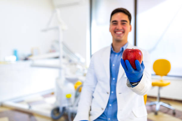 Young man dentist holding red apple and smiling