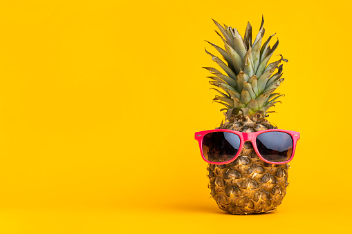 Pineapple with sunglasses on yellow background, summer vacation concept