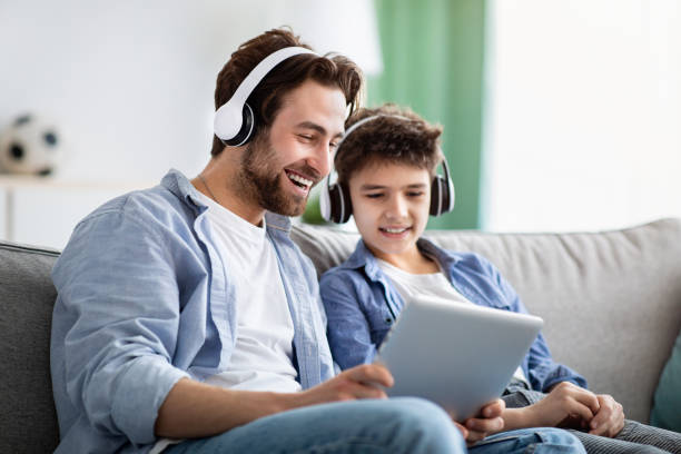 tecnologie moderne. allegro padre e figlio che guardano film su tablet digitale, indossando cuffie wireless - music listening child smiling foto e immagini stock