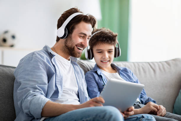 Modern technologies. Cheerful father and son watching film on digital tablet, wearing wireless headphones