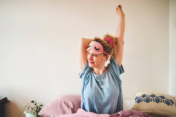 I'm awake and energized! Cropped shot of an attractive young woman sitting in bed and stretching after waking up in the morning waking up stock pictures, royalty-free photos & images