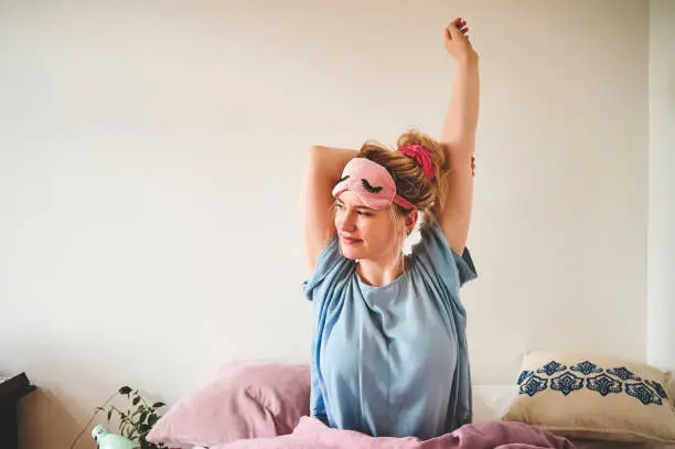 Cropped shot of an attractive young woman sitting in bed and stretching after waking up in the morning