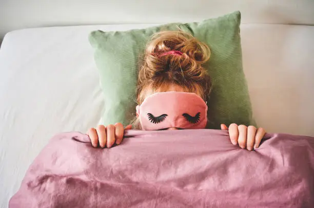 Cropped shot of an unrecongizable woman lying in bed with a sleep mask on and covering her face with her duvet