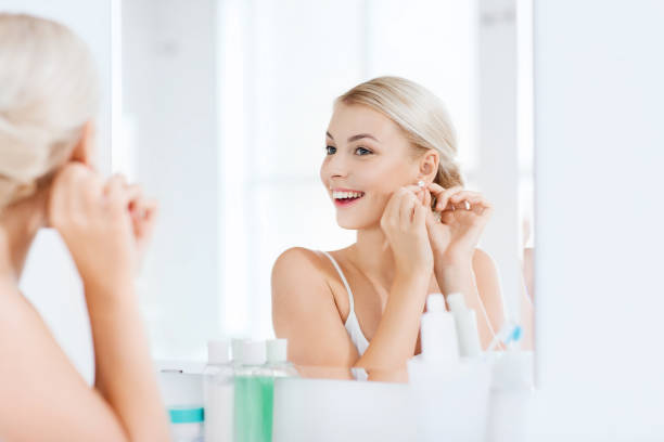 woman trying on earring looking at bathroom mirror beauty, jewelry and people concept - smiling young woman trying on diamond earring and looking to mirror at home bathroom diamond earring stock pictures, royalty-free photos & images