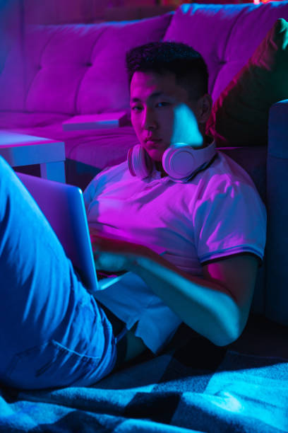 istock Young Korean man using laptop at home interior in gradient pink blue neon light 1312608452