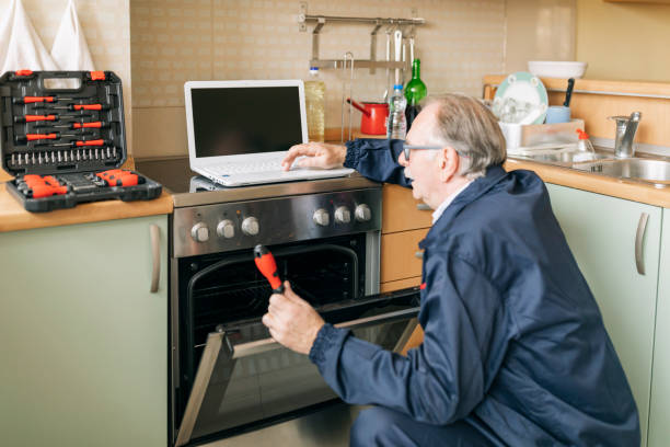 istock Senior Working Man is Fixing an Oven with a Screwdriver and Looking for Online Help. 1312608630