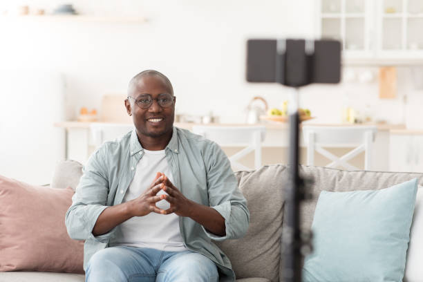 istock Mature african american blogger broadcasting from home, using smartphone and tripod, talking and gesturing to cellphone 1312609360