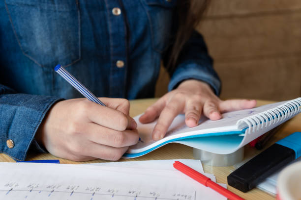 istock Girl in a blue denim shirt sitting in a cafe makes notes in a notepad with a pen. A sheets with emotions schedule, adhesive tape, felt-tip pens are on the table. Close up 1312609752