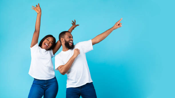 istock Smiling black couple celebrating win, pointing aside at copy space 1312611146