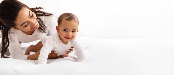 Black Mom Posing With Baby Toddler On White Studio Background Black Mom Posing With Baby Toddler Holding Helping Her Son Crawl On White Studio Background. Happy Young Mother Caring For Child Infant Bonding And Playing With Cute Little Boy. Panorama, Copy Space nanny photos stock pictures, royalty-free photos & images