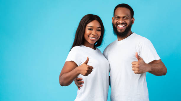 Happy black couple gesturing thumbs up, hugging and smiling, banner Family Approval. Smiling black couple hugging and showing thumbs up sign gesture. Young man and woman posing and looking at camera isolated over blue studio background, banner, free copy space couple hope sky blue stock pictures, royalty-free photos & images