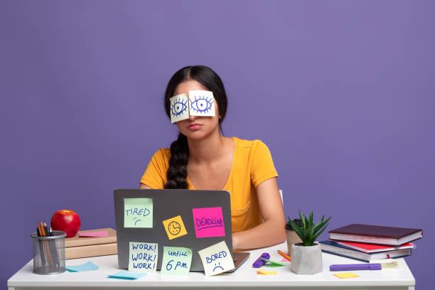 Tired woman sitting at desk with sticky notes on eyes