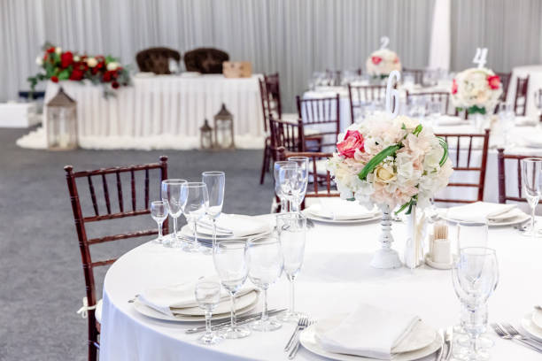istock Fancy table set for dinner with flower composition in restaurant, luxury interior background. Wedding elegant banquet decoration and items for food arranged by catering service on white table 1312615094