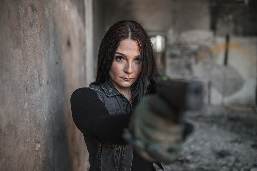 Young woman mercenary assassin with gun in war zone in abandoned warehouse