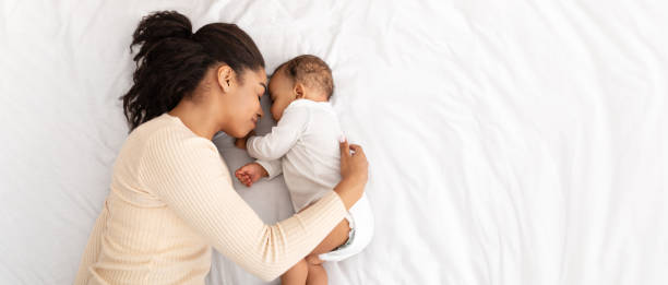madre africana abrazando bebé dormido acostado en la cama en interior, alto ángulo - bebé fotografías e imágenes de stock