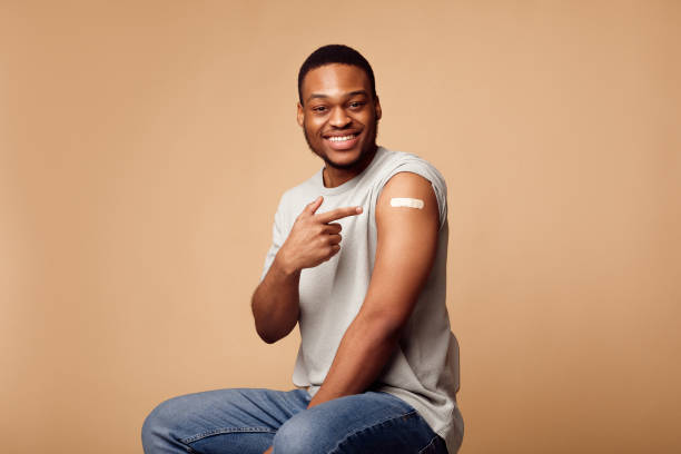 istock African Guy Pointing Finger At Vaccinated Arm Sitting, Beige Background 1312616833