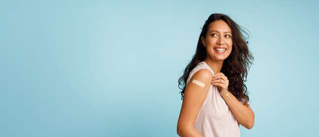Mujer mostrando brazo vacunado con vendaje después de la inyección, fondo azul photo
