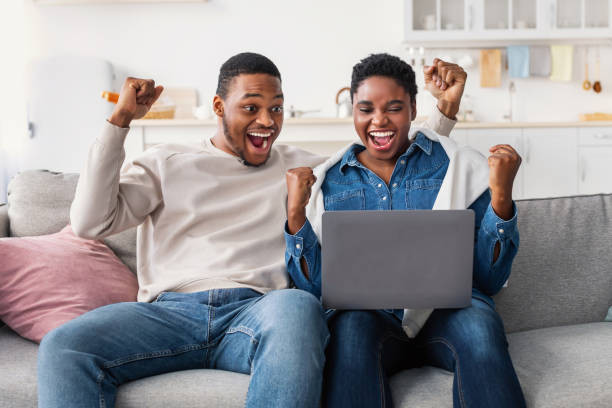 pareja negra usando portátil celebrando el éxito sacudiendo puños - shaking fist fotografías e imágenes de stock