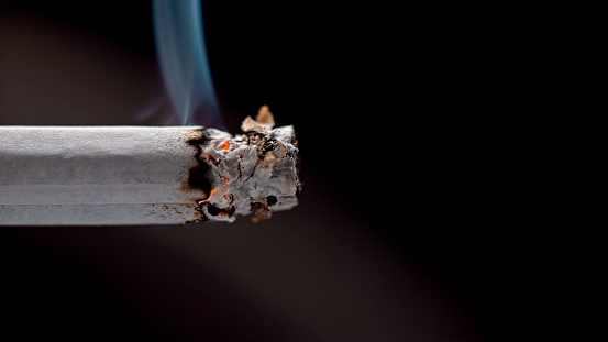 Close-up of burning cigarette with smoke against black background.