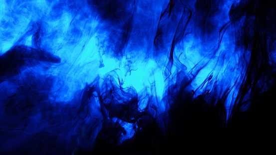 Close-up of blue colored paint dissolving in water against black background.