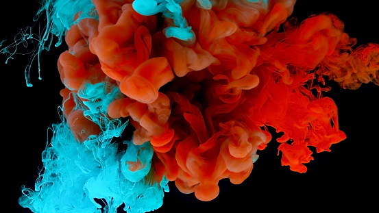 Close-up of orange and turquoise colored paints dissolving in water against black background.