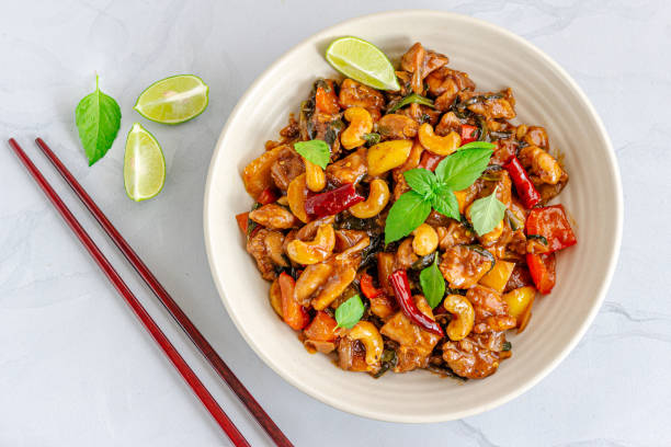 Stir-Fried Cashew Chicken in a Bowl Garnished with Fresh Thai Basil and Lemon