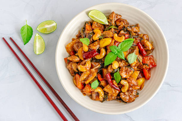 Stir-Fried Cashew Chicken in a Bowl Garnished with Fresh Thai Basil and Lemon stock photo