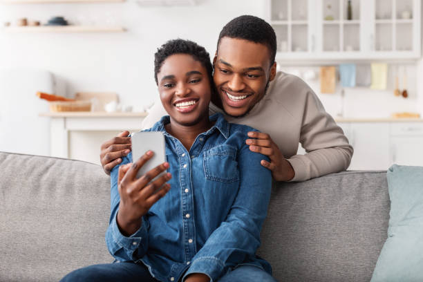 istock Black couple sitting on couch, using smartphone 1312622341