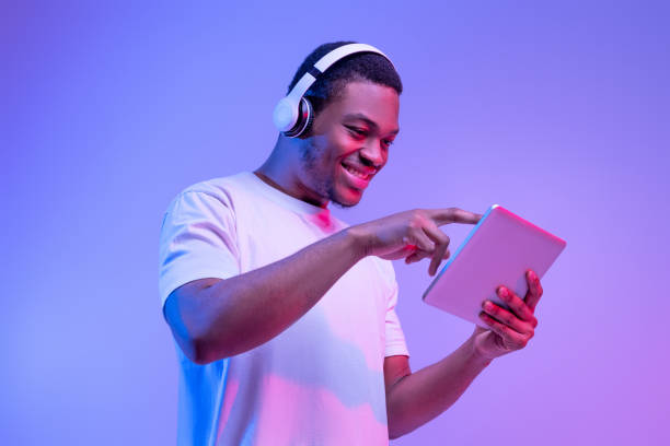 istock Interesting App. Excited African American Guy In Wireless Headphones Using Digital Tablet 1312622754