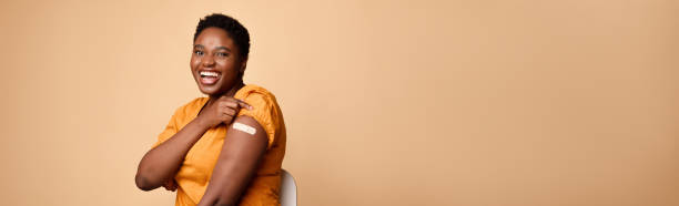 African Female Rolling Up Sleeves Showing Vaccinated Arm, Beige Background Successful Covid-19 Vaccination. Joyful African Female Rolling Up Sleeves Showing Vaccinated Arm With Plaster Sitting On Beige Background. Coronavirus Immunization Campaign. Panorama, Free Space adhesive bandage stock pictures, royalty-free photos & images