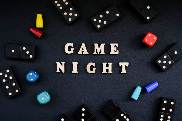 text game night spelled out in wooden letter. surrounded by dice, dominoes other game pieces on black background. table games. stay home activity - night piece imagens e fotografias de stock