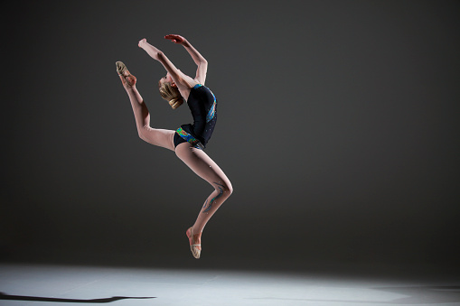 Rhytmic gymnastics female routine on dark background. Figure jump.