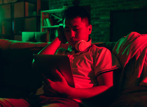 istock Young Korean man using tablet at home interior in gradient red green neon light 1312629962