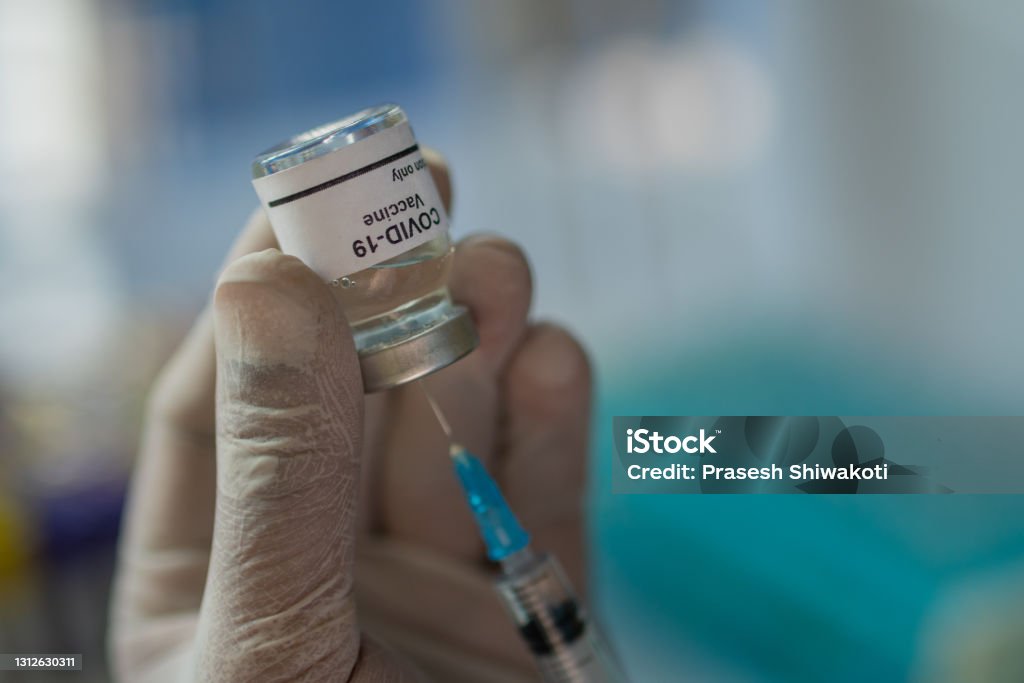 Coronavirus Covid-19 Vaccine - stock photo A health care worker wearing gloves and holding a Covid-19 vaccine vial and a syringe - stock photo. Anti-vaccination Stock Photo