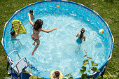 A high view of a girl leaping into a sparkling swimming pool while her siblings stay out of her way