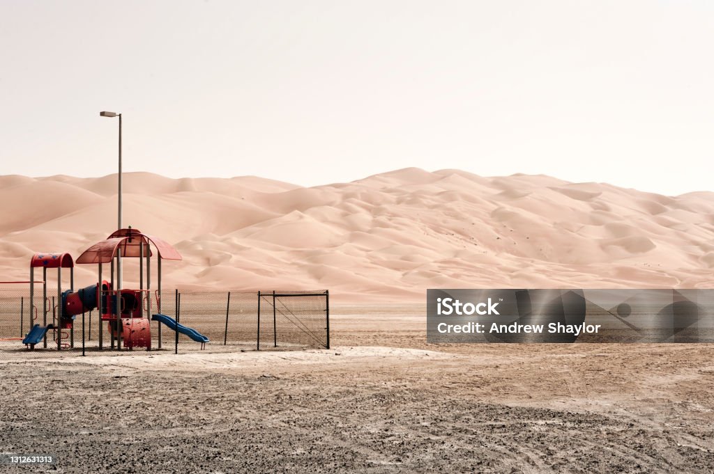 Playground and Moreeb Dune in Liwa desert A deserted playground in the shadow of Moreeb Dune in Liwa desert. Arid Climate Stock Photo