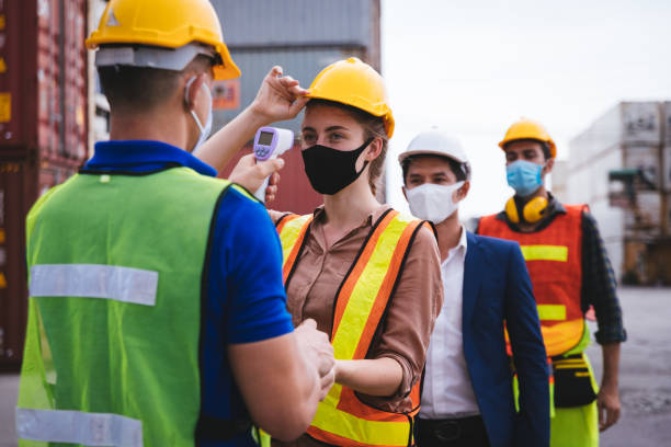 istock Worker scanning fever temperature with digital thermometer to construction site staff wearing hygiene face mask protect from Coronavirus or COVID-19. New Normal working life adaptation in 2020 1312635947