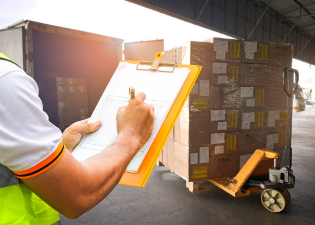 istock Worker Holding Clipboard and Writing on Paper. Ckecking Order Package Boxes. Shipment Boxes Loading into Container Truck at Dock Warehouse. 1312638905