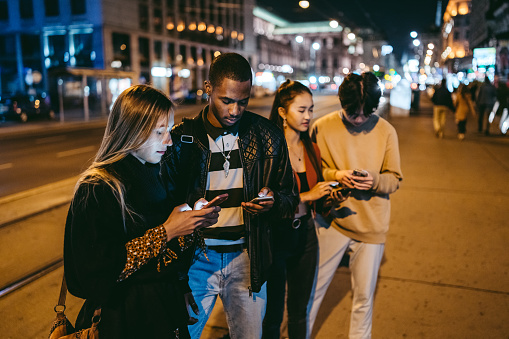 Group of multi-ethnic teenagers using phones on the street.