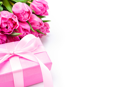 Composition of a pink gift box and tulips bouquet at the left of a white background leaving room for text and/or logo. Predominant colors are pink and white. High resolution 42Mp studio digital capture taken with SONY A7rII and Zeiss Batis 40mm F2.0 CF lens