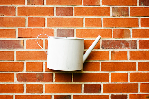 White metal watering can on red brick wall background