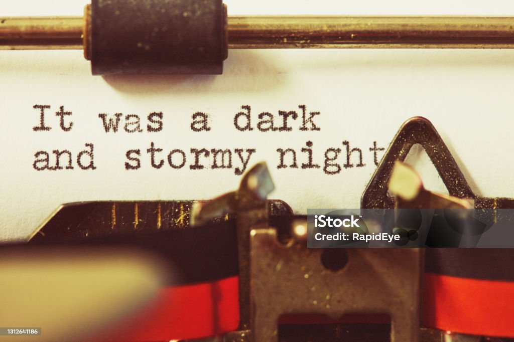 Close-up of paper in an old-fashioned typewriter begins a piece of writing with a well-known cliche Retro typewriter types It was a dark and stormy night. Author Stock Photo
