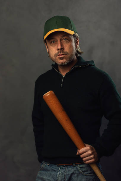 istock Blond man with baseball cap and bat in a dark green wool sweater. 1312641435